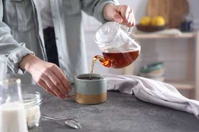 Photo of Woman pouring hot tea into cup at grey table, closeup