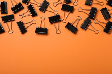 Photo of Black binder clips on orange background, flat lay. Space for text