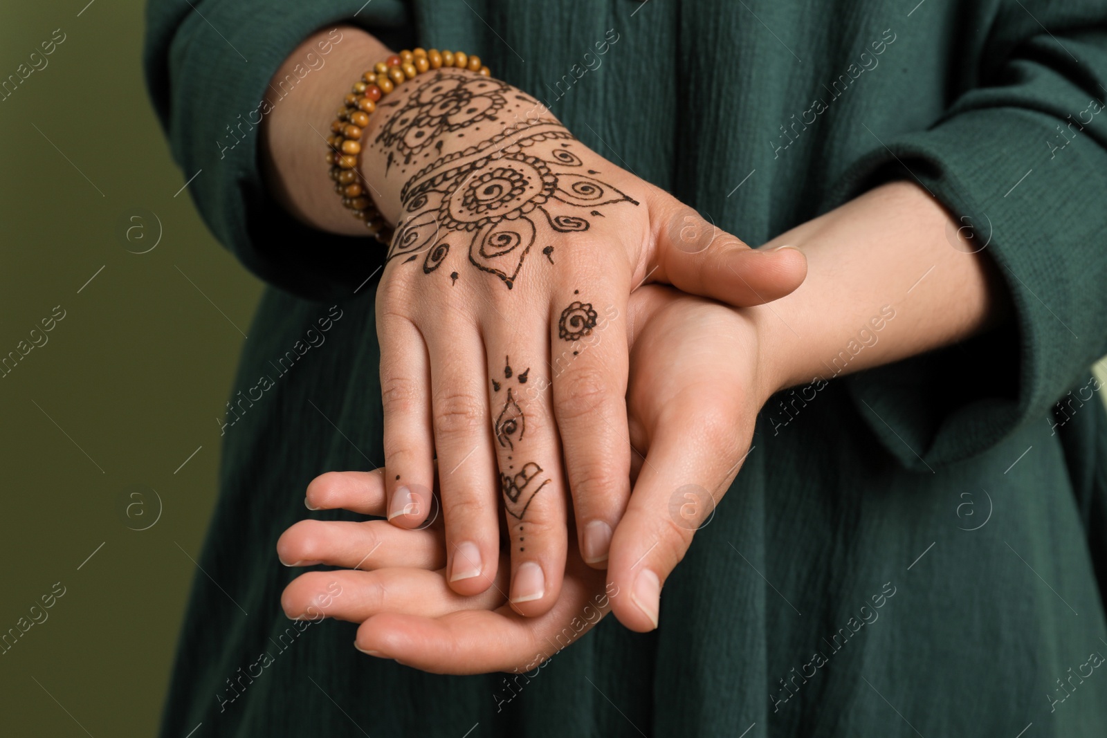Photo of Woman with beautiful henna tattoo on hand against green background, closeup. Traditional mehndi
