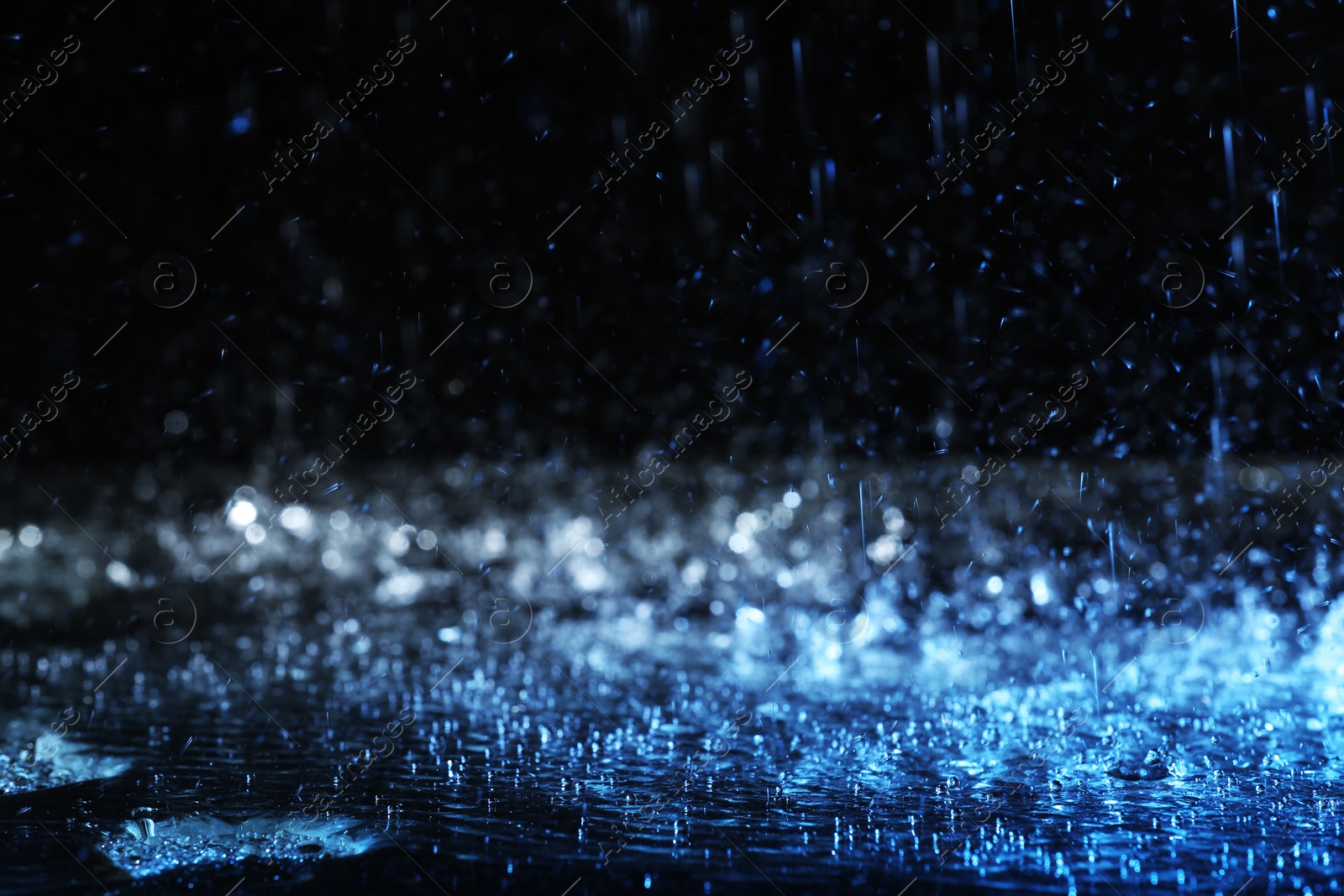 Photo of Heavy rain falling down on ground against dark background, toned in blue