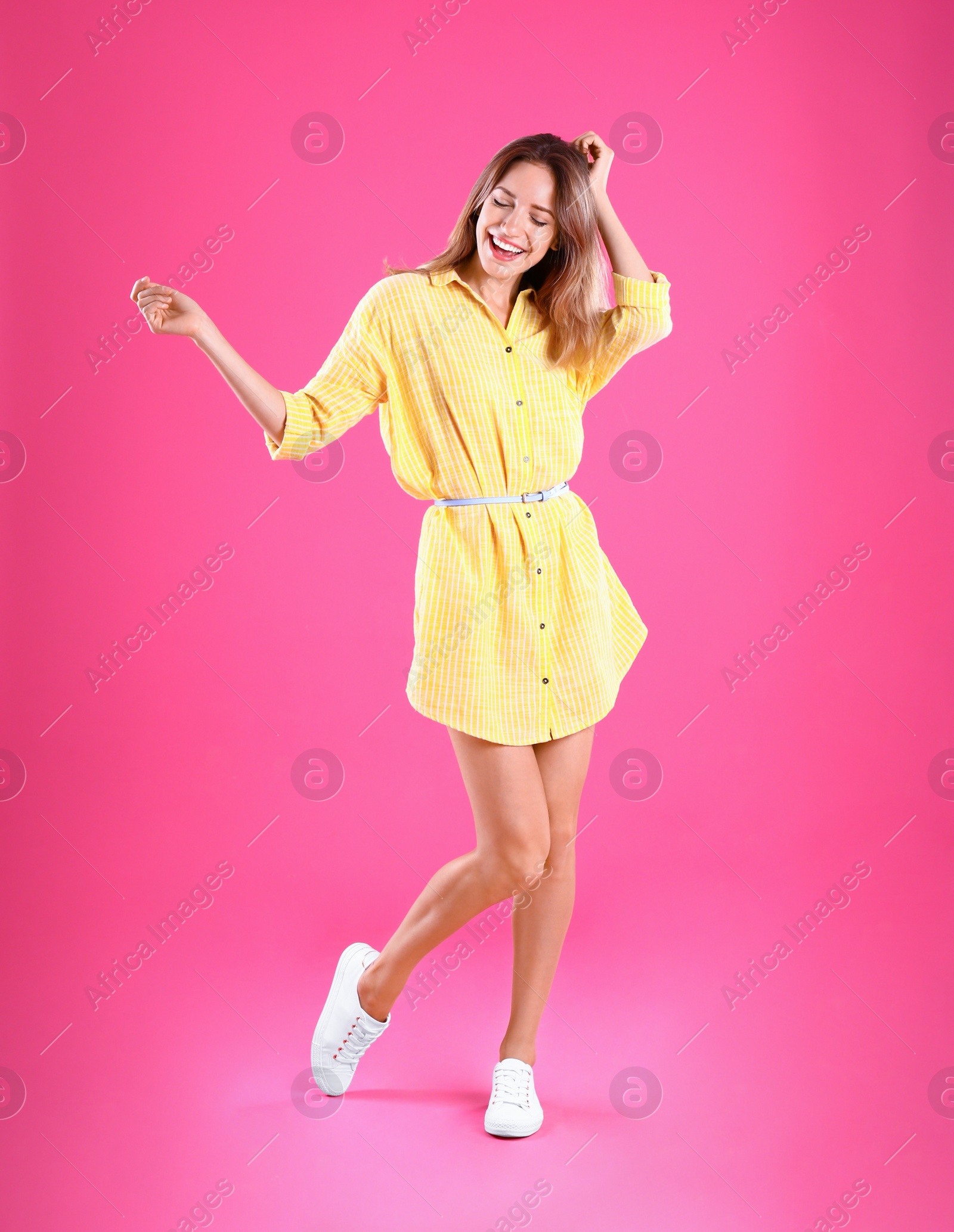 Photo of Beautiful young woman in yellow dress dancing on pink background