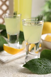 Photo of Tasty limoncello liqueur and green leaves on light textured table, closeup
