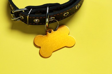 Photo of Black leather dog collar with golden tag in shape of bone on yellow background, closeup. Space for text