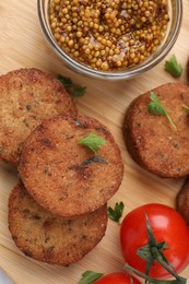 Tasty vegan cutlets, tomato and grain mustard on wooden table, flat lay