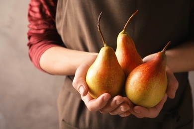 Woman holding ripe pears on grey background, closeup