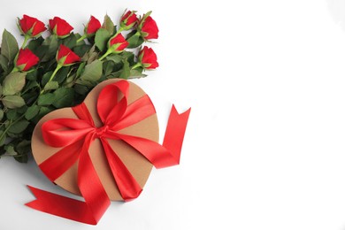 Photo of Heart shaped gift box with bow and beautiful red roses on white background, flat lay. Space for text