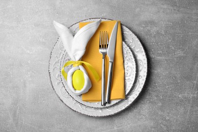 Photo of Festive table setting with bunny made of painted egg and napkin on light grey background, flat lay. Easter celebration