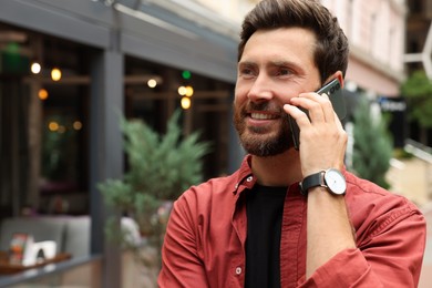 Photo of Handsome man talking on smartphone while walking outdoors, space for text