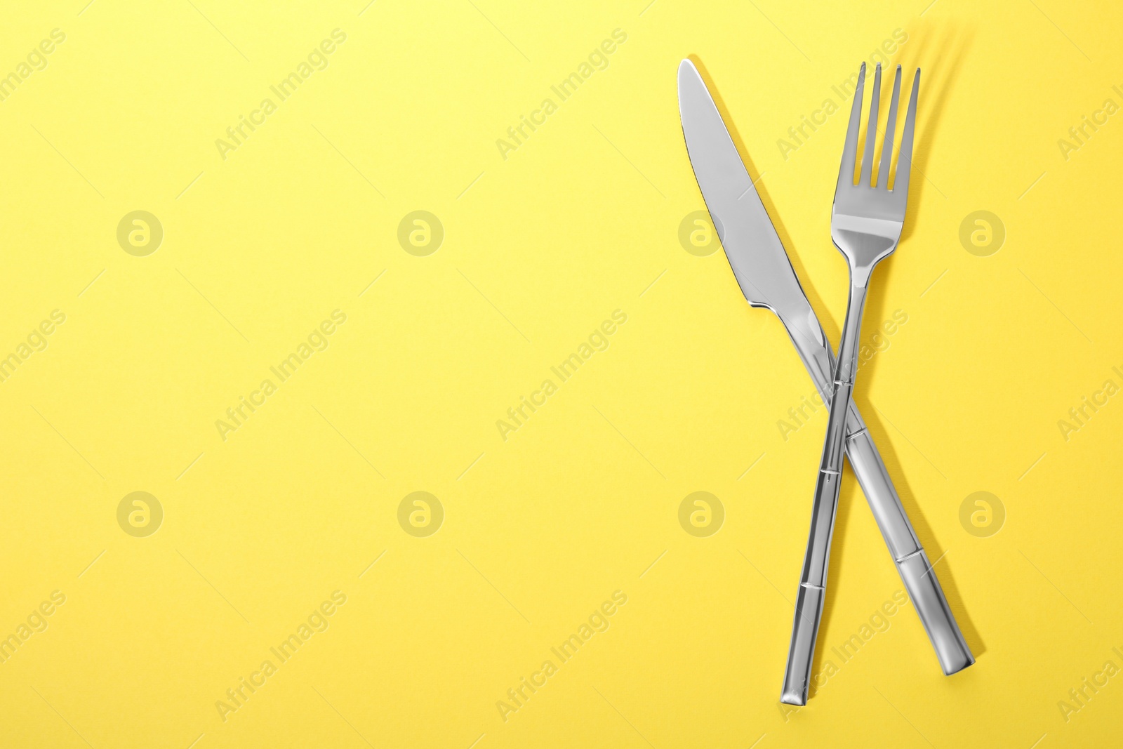 Photo of Shiny fork and knife on yellow background, flat lay. Space for text