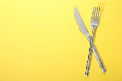 Shiny fork and knife on yellow background, flat lay. Space for text