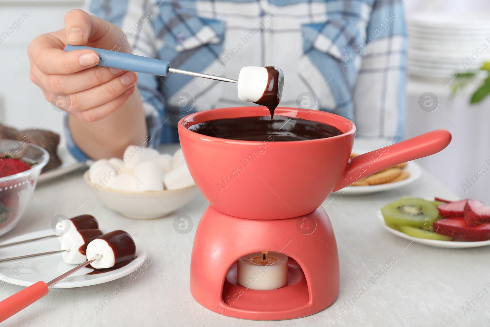 Photo of Woman dipping marshmallow into pot with chocolate fondue at table, closeup