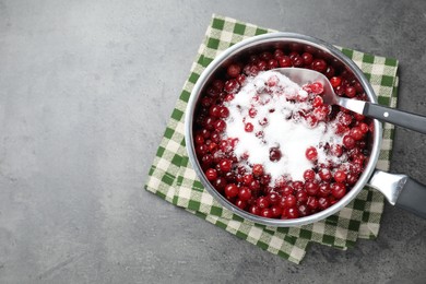 Photo of Making cranberry sauce. Fresh cranberries with sugar in saucepan and spoon on gray table, top view. Space for text