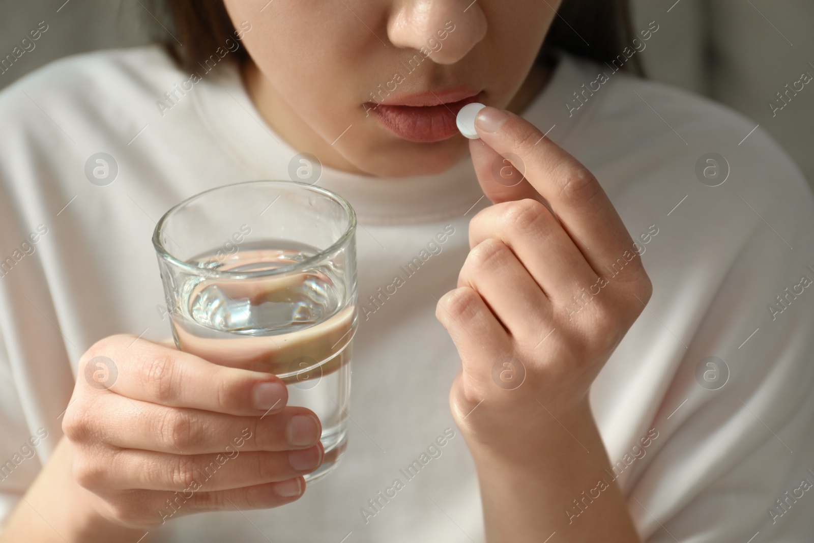 Photo of Young woman taking abortion pill on light background, closeup