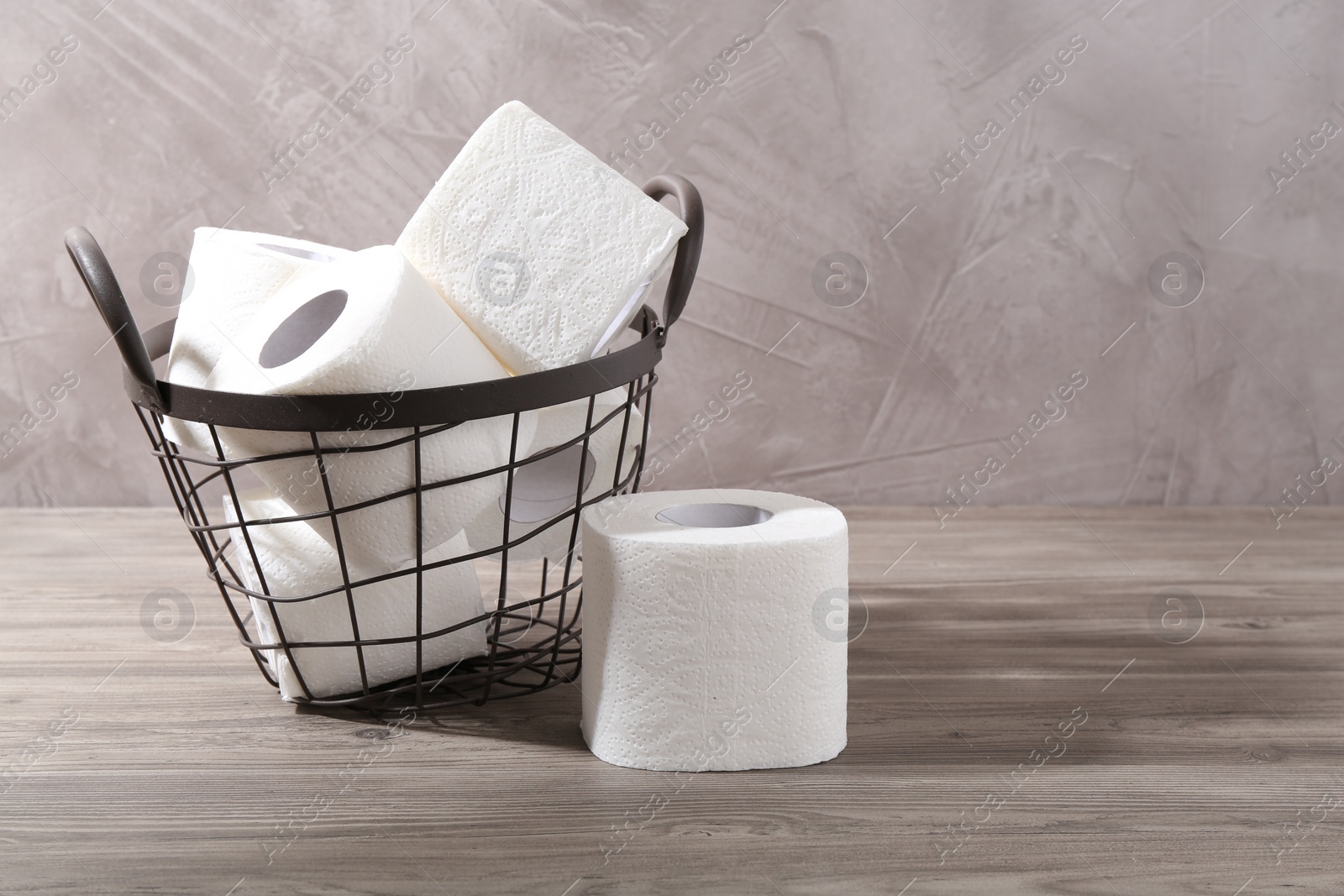 Photo of Soft toilet paper rolls in metal basket on wooden table, closeup. Space for text