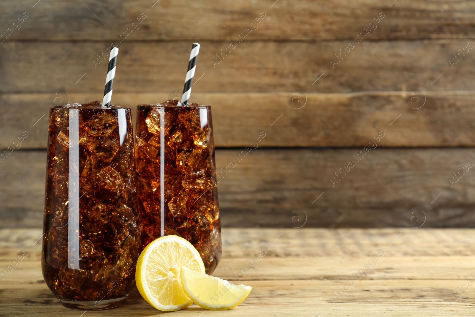 Photo of Glasses of refreshing soda water with ice cubes and lemon on wooden table, space for text