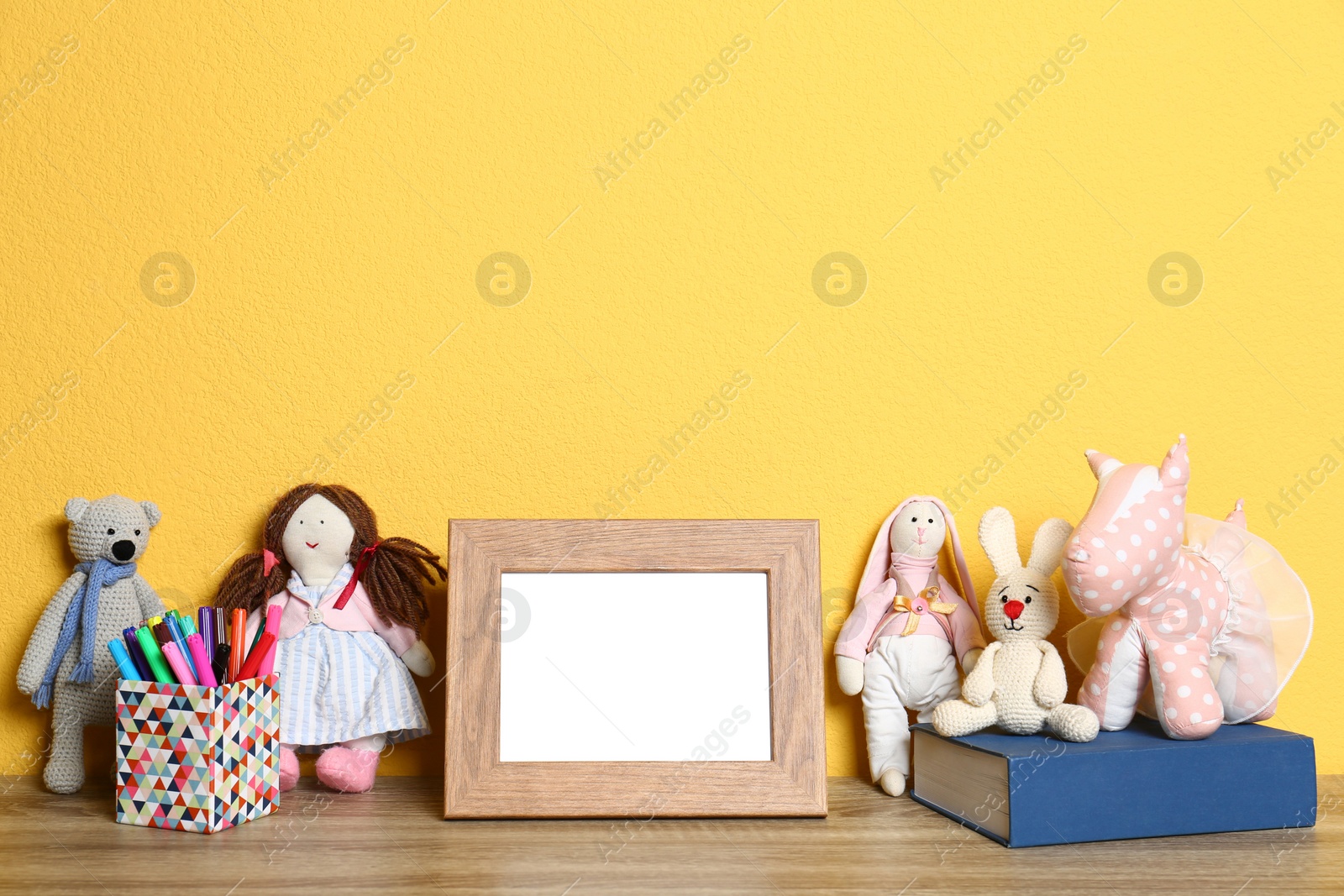 Photo of Soft toys and photo frame on table against yellow background, space for text. Child room interior