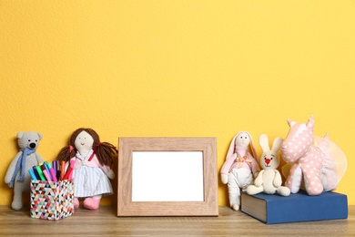 Photo of Soft toys and photo frame on table against yellow background, space for text. Child room interior