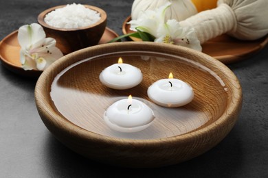 Photo of Spa composition with burning candles in bowl with water on grey table