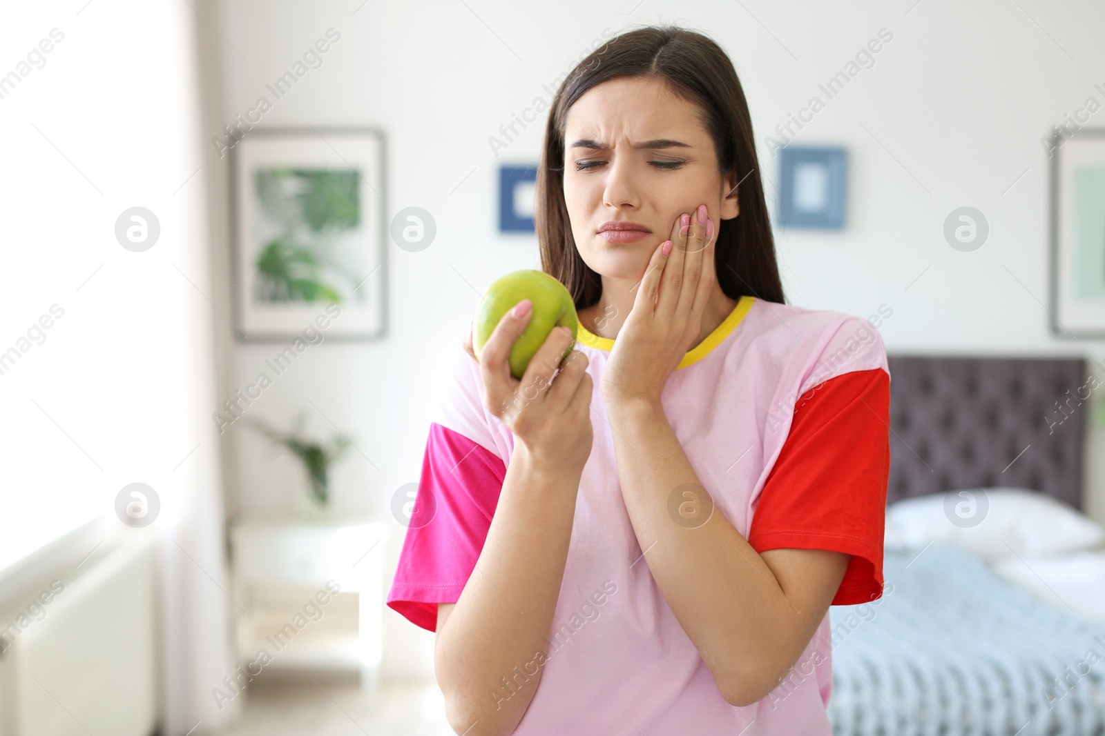 Photo of Young woman with sensitive teeth and apple at home