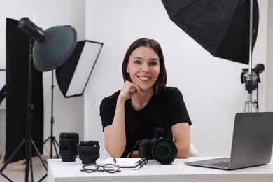 Young professional photographer with camera at table in modern photo studio