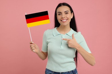 Happy young woman pointing at flag of Germany on pink background