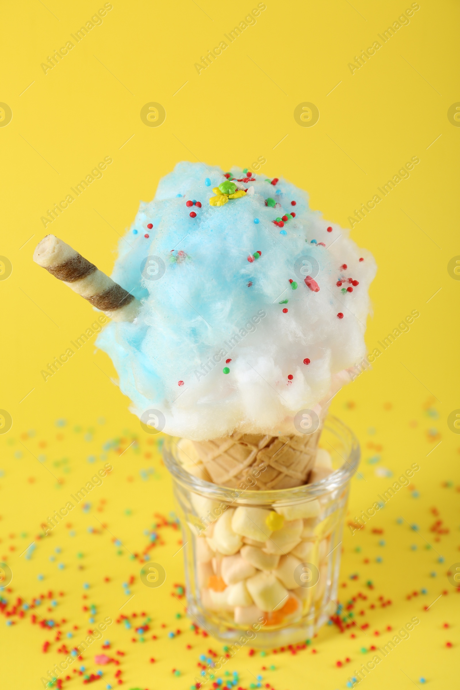 Photo of Sweet cotton candy in waffle cone on yellow background, closeup