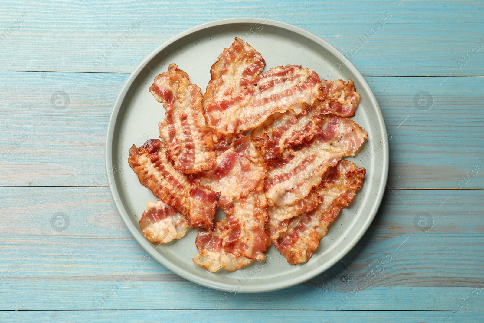 Photo of Delicious fried bacon slices on blue wooden table, top view