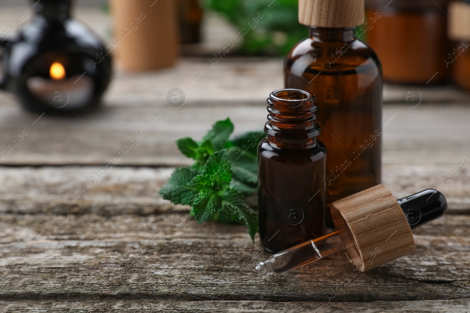 Photo of Bottles of mint essential oil and fresh leaves on wooden table, closeup. Space for text