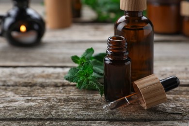 Photo of Bottles of mint essential oil and fresh leaves on wooden table, closeup. Space for text