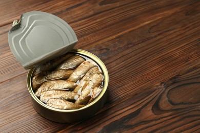 Open tin can of sprats on wooden table. Space for text