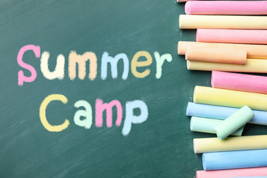 Image of Pieces of color chalk and text SUMMER CAMP written on green chalkboard, flat lay