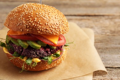 Photo of Tasty vegetarian burger with beet cutlet, cheese, avocado and tomato on wooden table, closeup. Space for text
