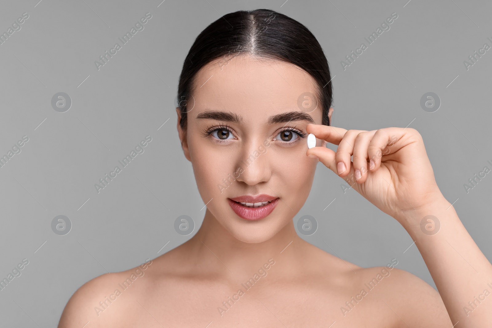 Photo of Beautiful young woman with vitamin pill on grey background