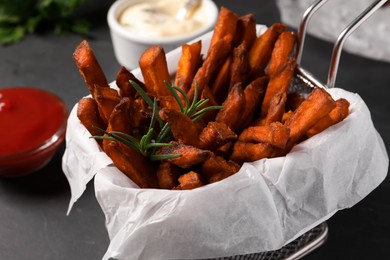 Photo of Frying basket with sweet potato fries and sauces on black table, closeup