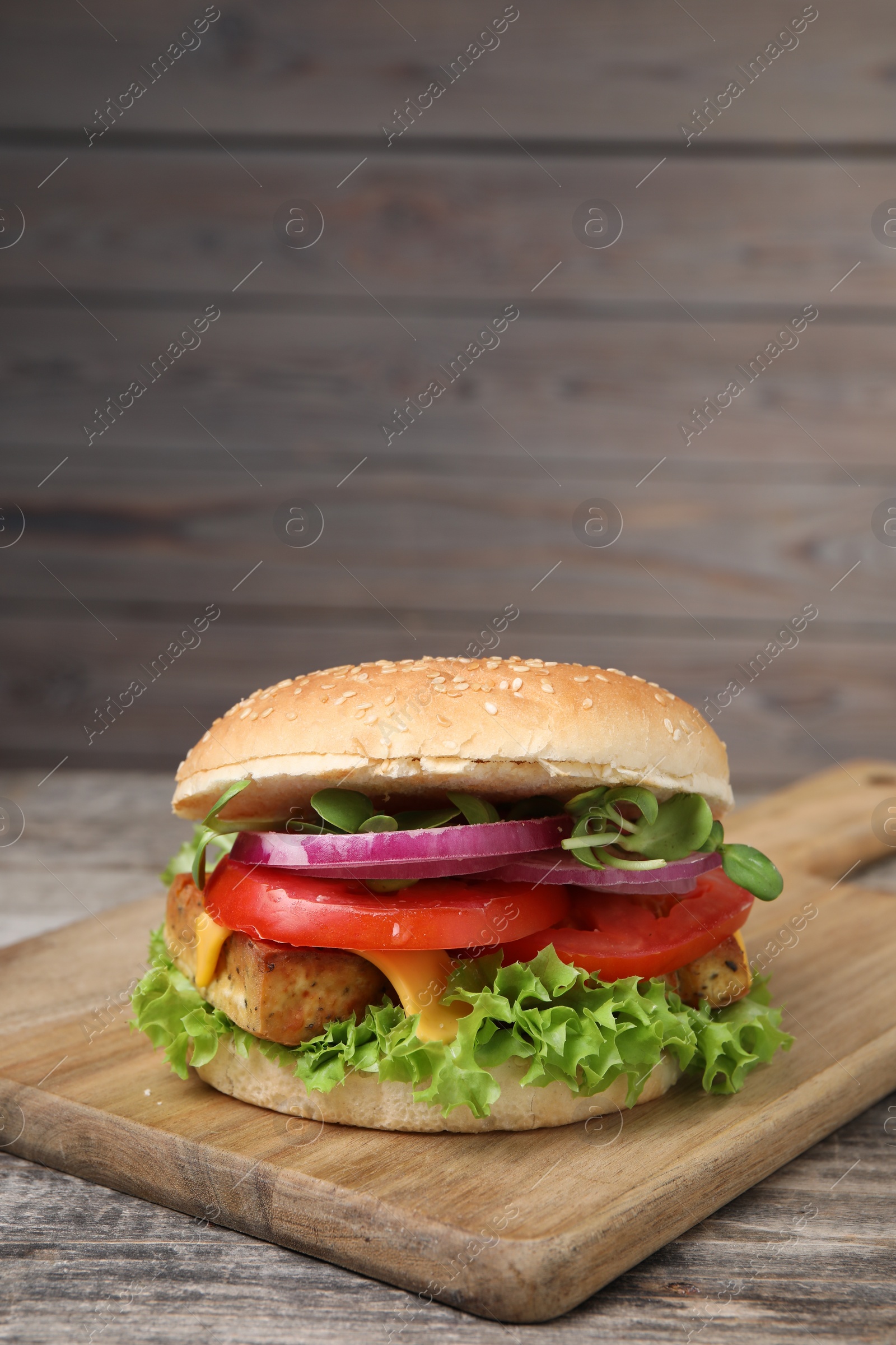 Photo of Delicious burger with tofu and fresh vegetables on wooden table, space for text