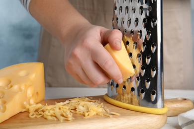 Woman grating fresh cheese at table, closeup