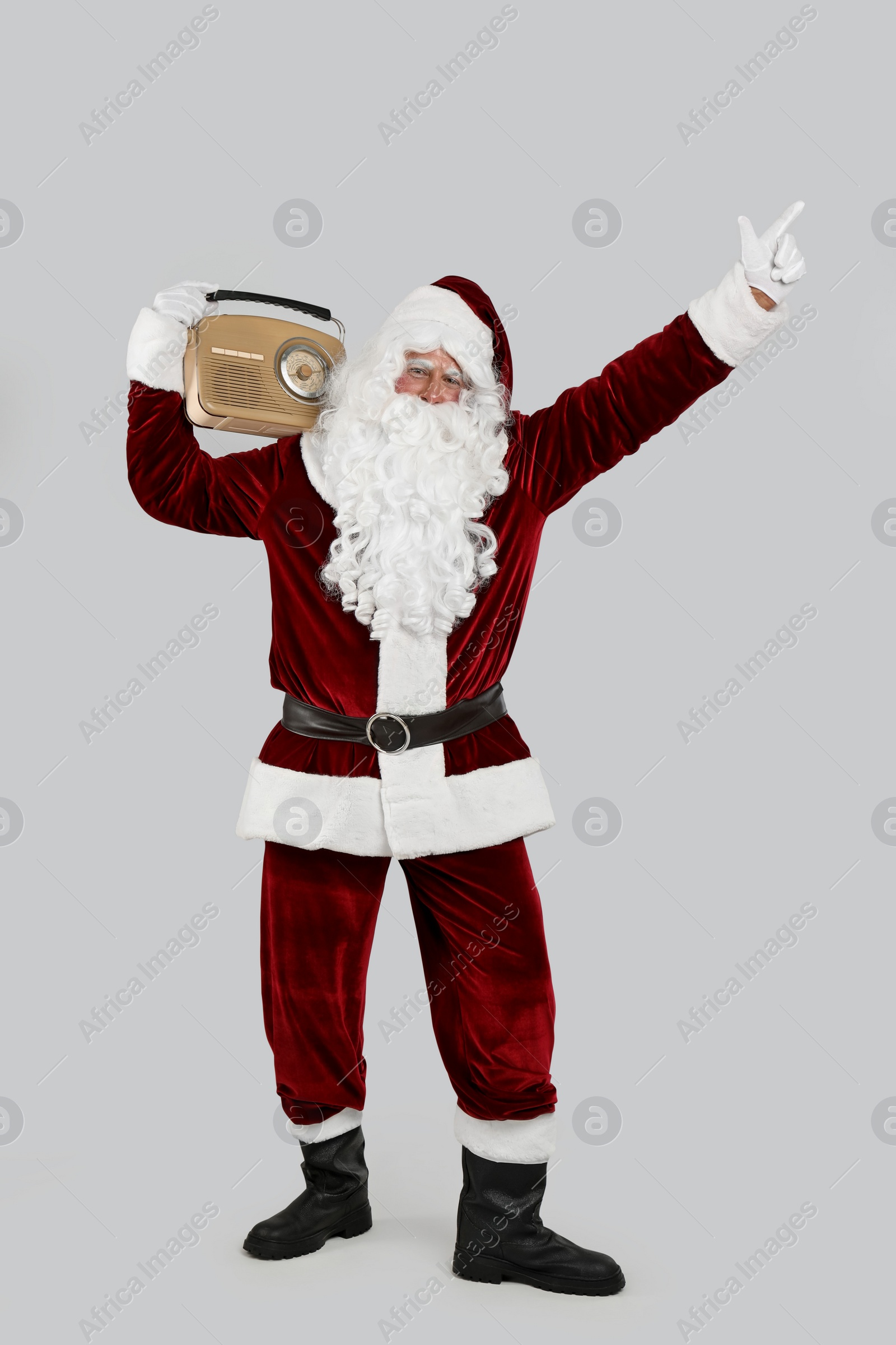 Photo of Santa Claus with vintage radio on light grey background. Christmas music