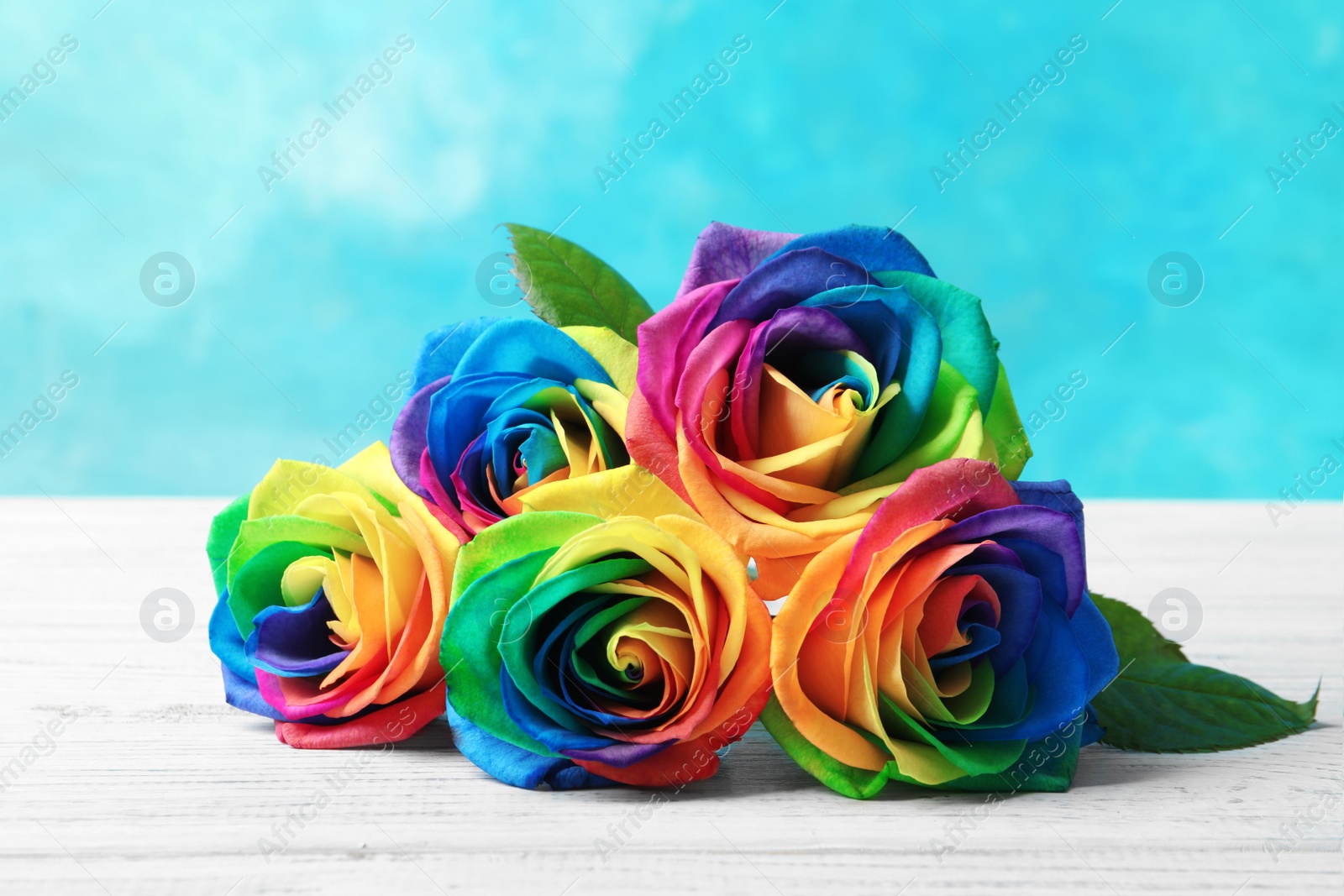 Photo of Rainbow rose flowers on table against color background