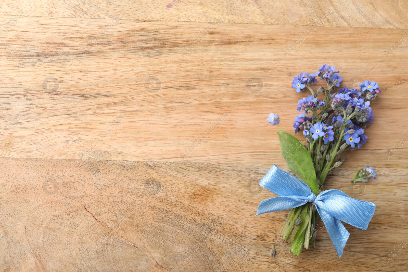 Photo of Beautiful blue forget-me-not flowers tied with ribbon on wooden table, top view. Space for text