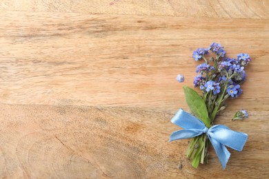 Photo of Beautiful blue forget-me-not flowers tied with ribbon on wooden table, top view. Space for text