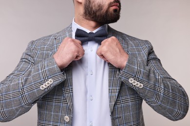 Photo of Man adjusting bow tie on grey background, closeup