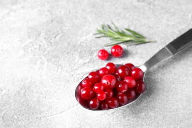 Photo of Fresh ripe cranberries in spoon on grey table, closeup. Space for text
