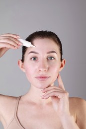 Young woman with acne problem applying cosmetic product onto her skin on light grey background