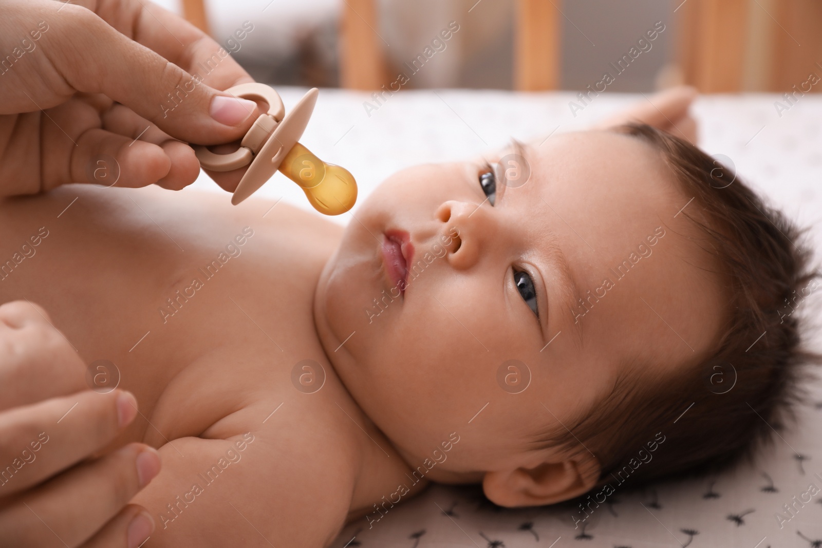 Photo of Mother giving pacifier to her cute little baby in crib at home, closeup