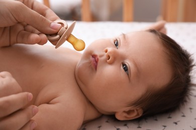 Mother giving pacifier to her cute little baby in crib at home, closeup