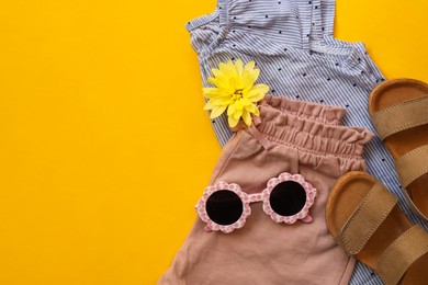 Stylish child clothes, shoes and sunglasses on yellow background, flat lay. Space for text