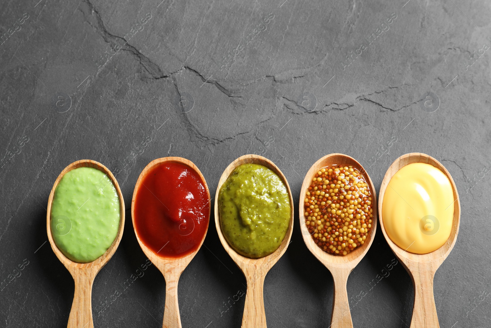 Photo of Set of wooden spoons with different delicious sauces on grey table, top view. Space for text