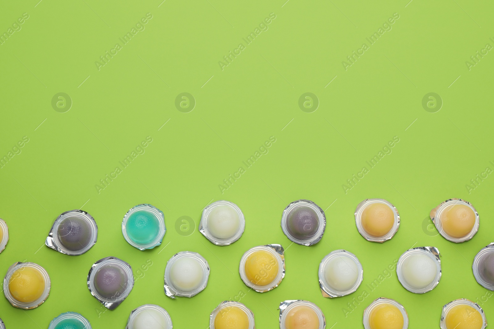 Photo of Tasty bright jelly cups on green background, flat lay. Space for text