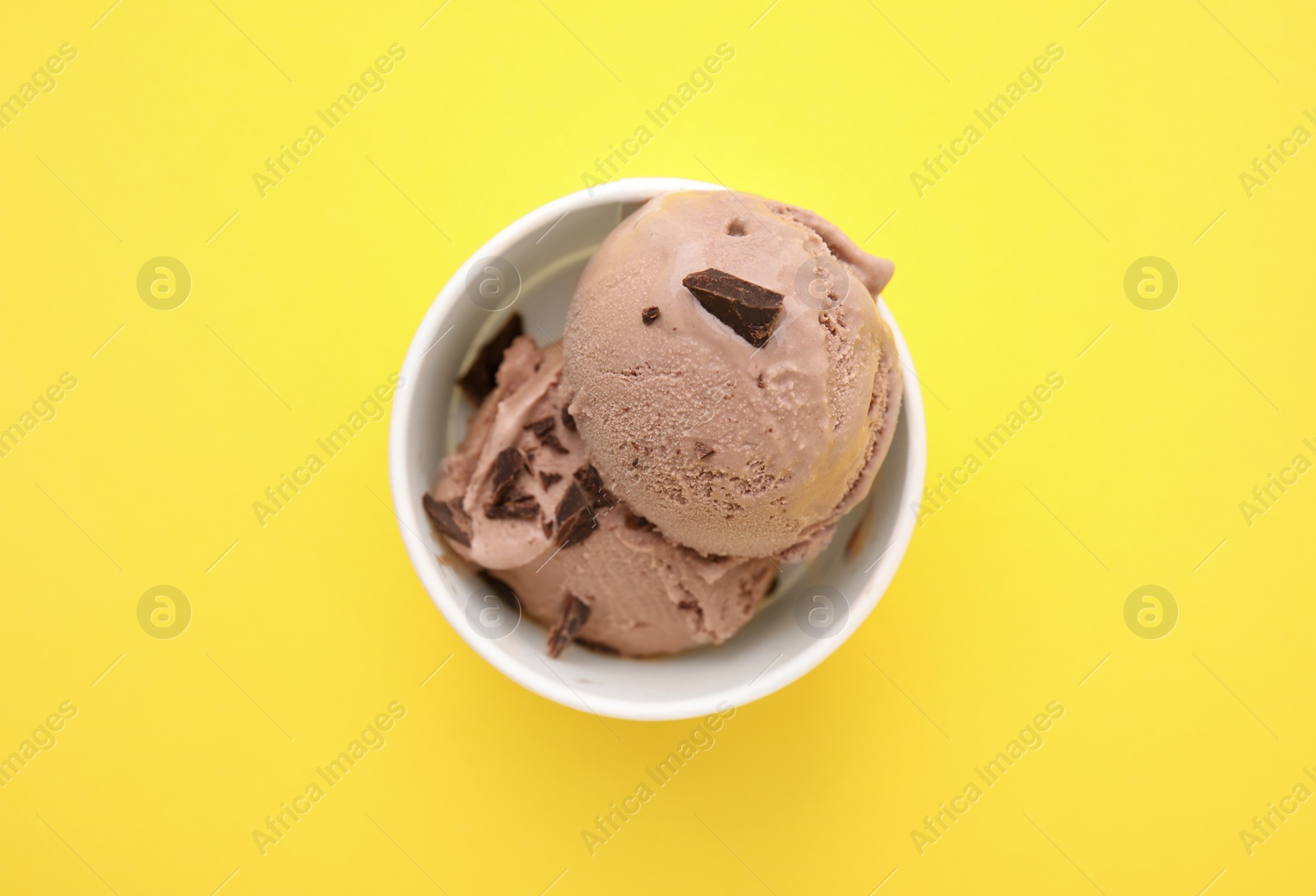 Photo of Cup with tasty chocolate ice cream on yellow background, top view