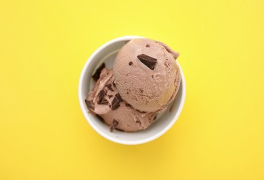 Cup with tasty chocolate ice cream on yellow background, top view